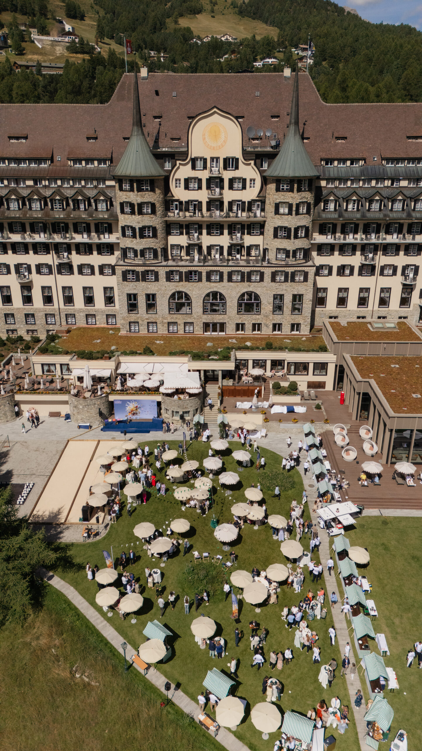 Luftaufnahme der St. Moritz Garden Party vor dem Suvretta House mit Sonnenschirmen auf der Wiese